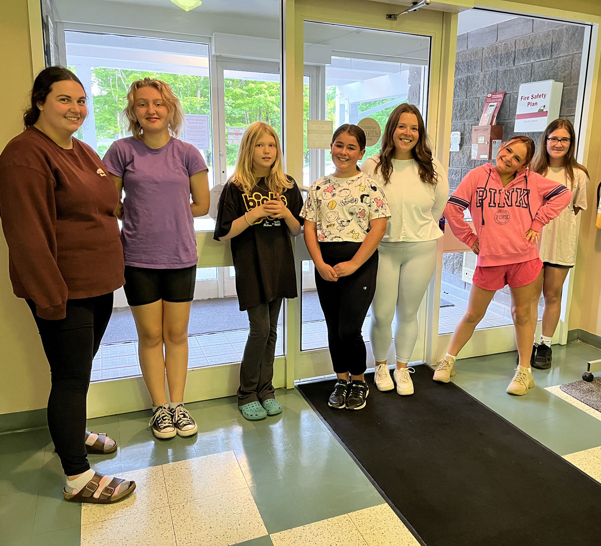 Seven women and girls smile for the camera wile standing in a bright hall inside a doorway.