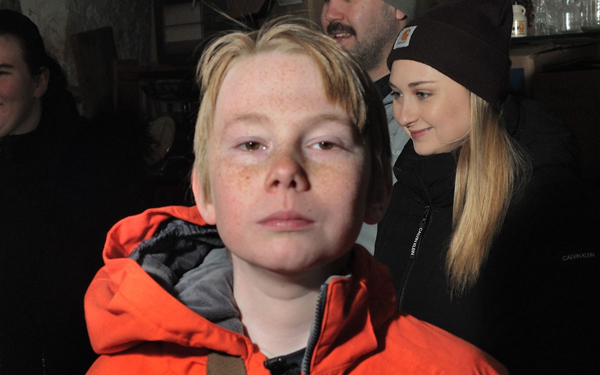 A red haired young boy in a red winter jacket looks at the camera