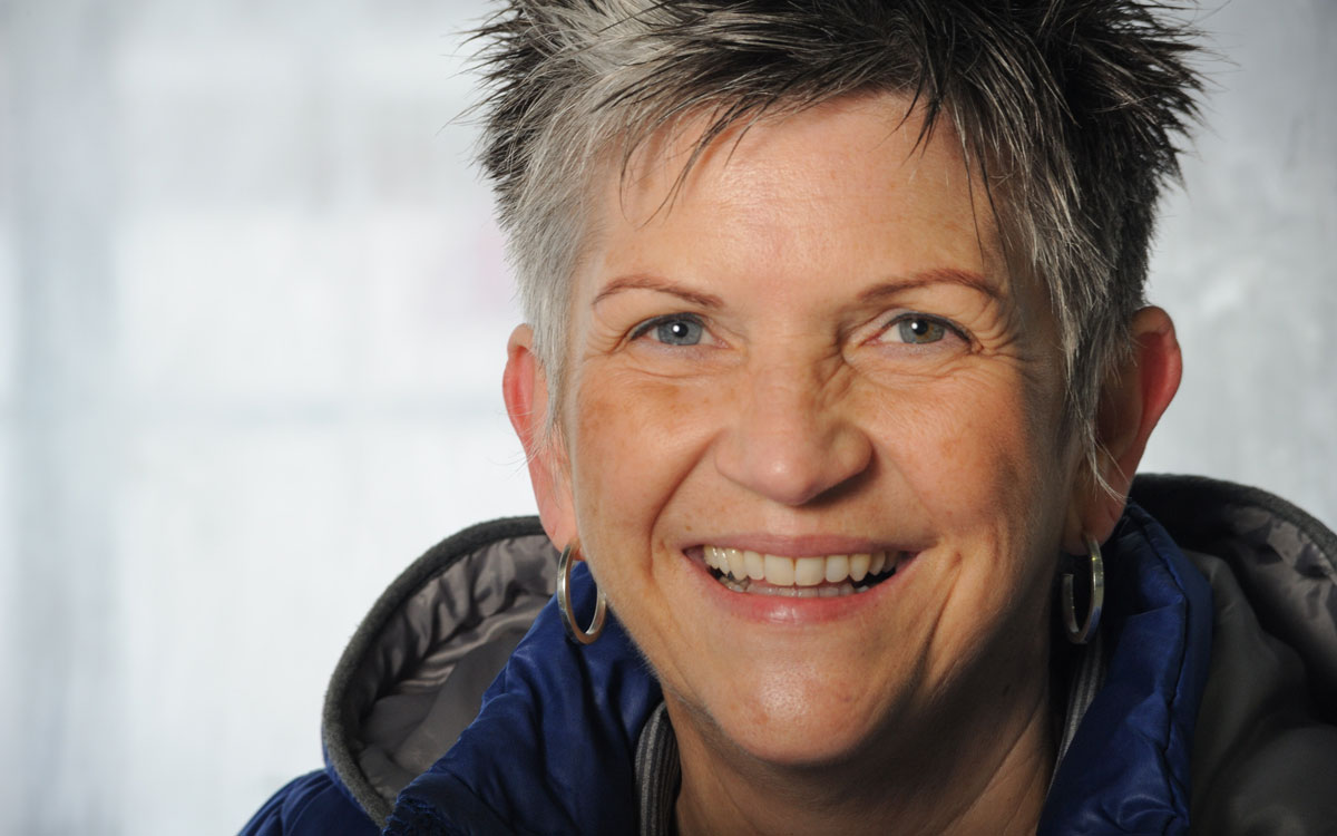 Close up of a smiling woman with short black and grey spiked hair and a big smail