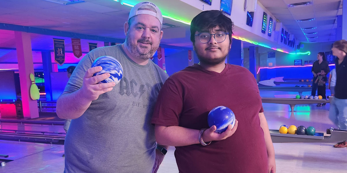 A man and an older teen at a neon glowing bowling lane holding bowling balls