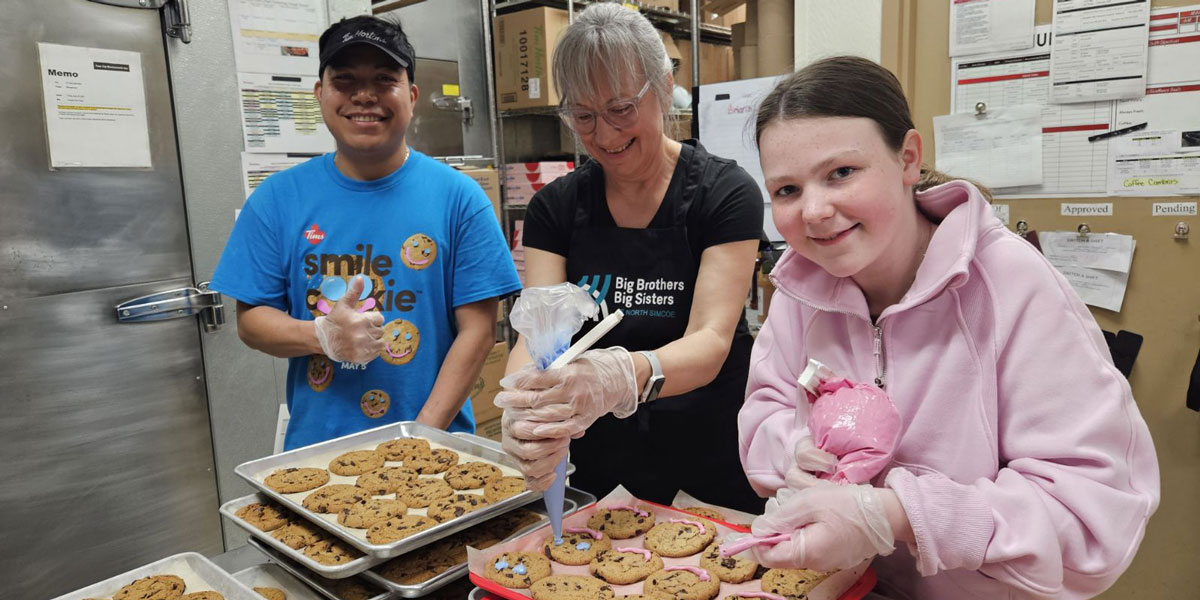 A young man, woman and your teen decorating chocolate chip cookies with icing bags.