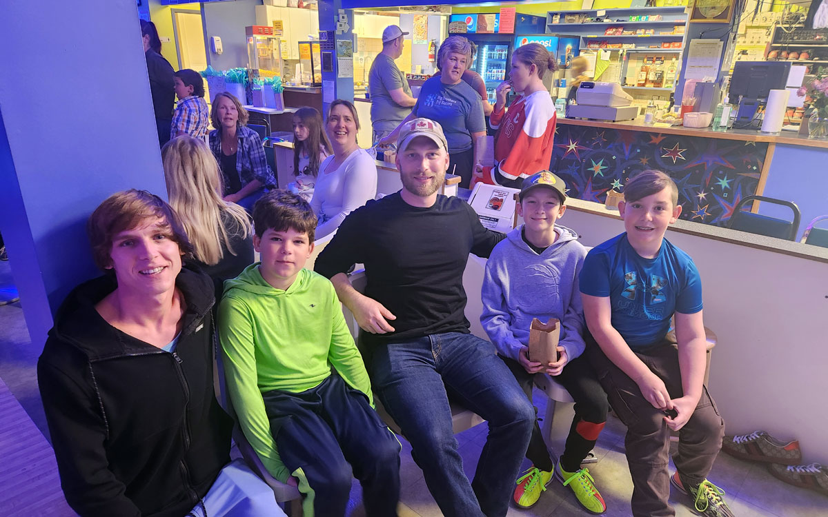 A group of adults and boys and girls of varying ages are sitting at a bowling alley.