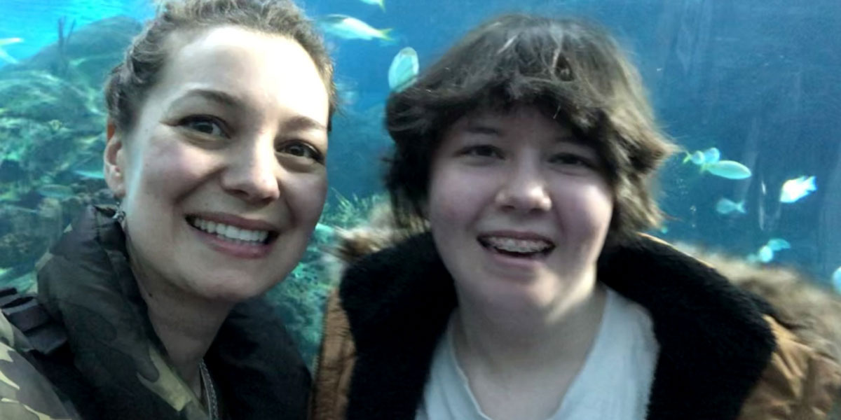 A woman and teen girl posw in front of a very large fish tank with fish